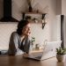 Free Young cheerful female smiling and talking via laptop while sitting at wooden table in cozy kitchen Stock Photo